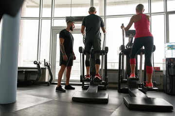 Seniors exercising on step machine with personal trainer