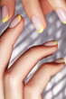 Hands with bright yellow french manicure. Nails art design. Close-up of hands with trendy neon nails on striped print