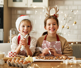 Poster - Happy children boy and girl smiling at camera while decorating Christmas gingerbreads in kitchen