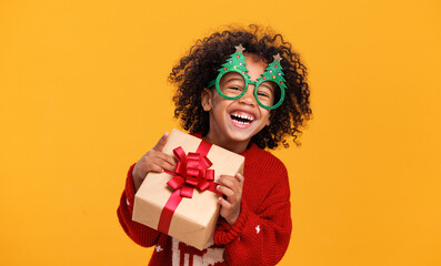 Happy little african american boy wearing funny glasses in form of Christmas trees with xmas gift