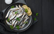 Salted sprat with lemon and parsley on a black background.
