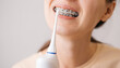 Smiling young unrecognizable woman with braces cleaning her teeth with oral irrigator. Dental and oral care.