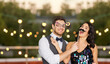 © Syda Productions - celebration, fun and holidays concept - happy couple posing with party props on roof top over lights on background
