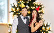 © Syda Productions - celebration and winter holidays concept - happy couple with party blowers and caps having fun over christmas tree lights background