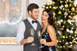 © Syda Productions - celebration and winter holidays concept - happy couple with glasses drinking non alcoholic champagne at party over christmas tree lights background