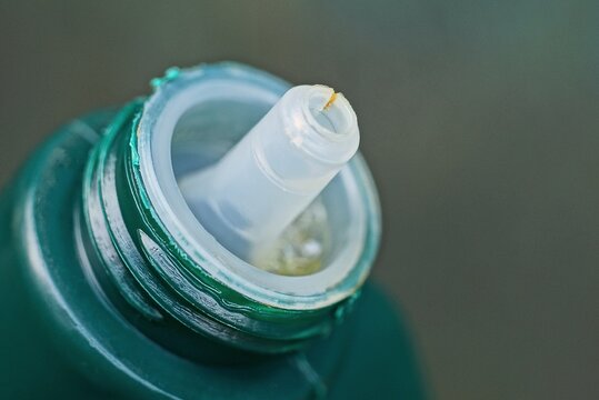 part of one green plastic bottle with white open cap on gray background