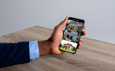 Wall Mural - Hand of caucasian man holding smartphone with views of home from security cameras on screen