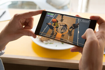 Canvas Print - Hands of caucasian man at restaurant watching basketball on smartphone