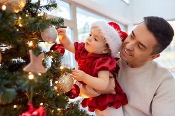 Poster - winter holidays and family concept - happy middle-aged father and baby daughter decorating christmas tree at home