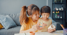Happy Cheerful Asia Family Mom Teach Toddler Girl Paint Ceramic Pot Having Fun Relax On Table In Living Room At House. Spending Time Together, Social Distance, Quarantine For Coronavirus Prevention.