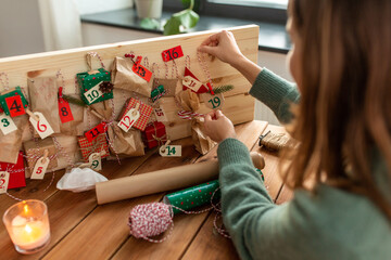 winter holidays, christmas and hobby concept - hands hanging gift with tag to handmade advent calendar at home