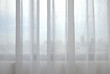 City center viewed through white voile window curtain
