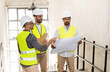 © Syda Productions - architecture, construction business and people concept - male architects in helmets with clipboard discussing blueprint in office building
