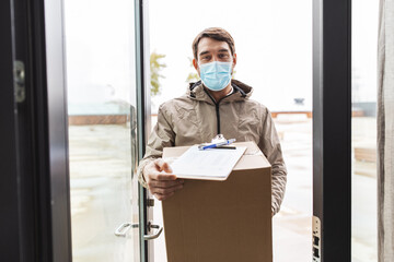 Sticker - health protection, safety and pandemic concept - delivery man in face protective mask holding parcel box with clipboard at open door