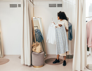 Wall Mural - Young woman choosing clothes while standing in fitting room in a boutique