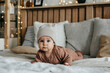 © Bostan Natalia - Baby lying on stomach on bed, wearing a knitted beanie with ears.