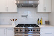 Modern kitchen details of white marble counter, gas stove, and white tile backsplash.