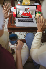 Canvas Print - Two waving men making laptop christmas video call with smiling senior african american santa claus