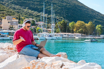 man freelancer working on laptop at city harbor bench