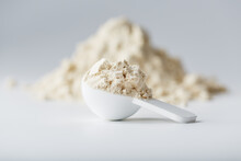 A Mountain Of Soy Protein Isolate In Powder With A Measuring Spoon On A White Background.