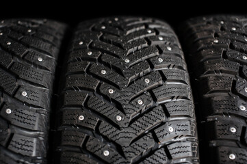 Wall Mural - New winter car tires with spikes close-up on a black background. Tire tread. Set of winter car tires