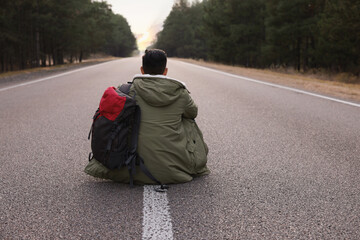 Wall Mural - Man with backpack sitting on road near forest, back view