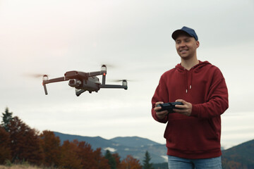 Wall Mural - Young man operating modern drone with remote control in mountains