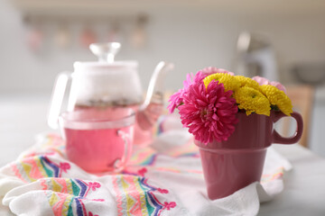 Canvas Print - Beautiful bright flowers in pink cup, fabric and aromatic tea on table indoors, space for text