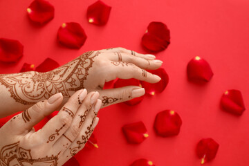 Wall Mural - Beautiful female hands with henna tattoo and rose petals on red background