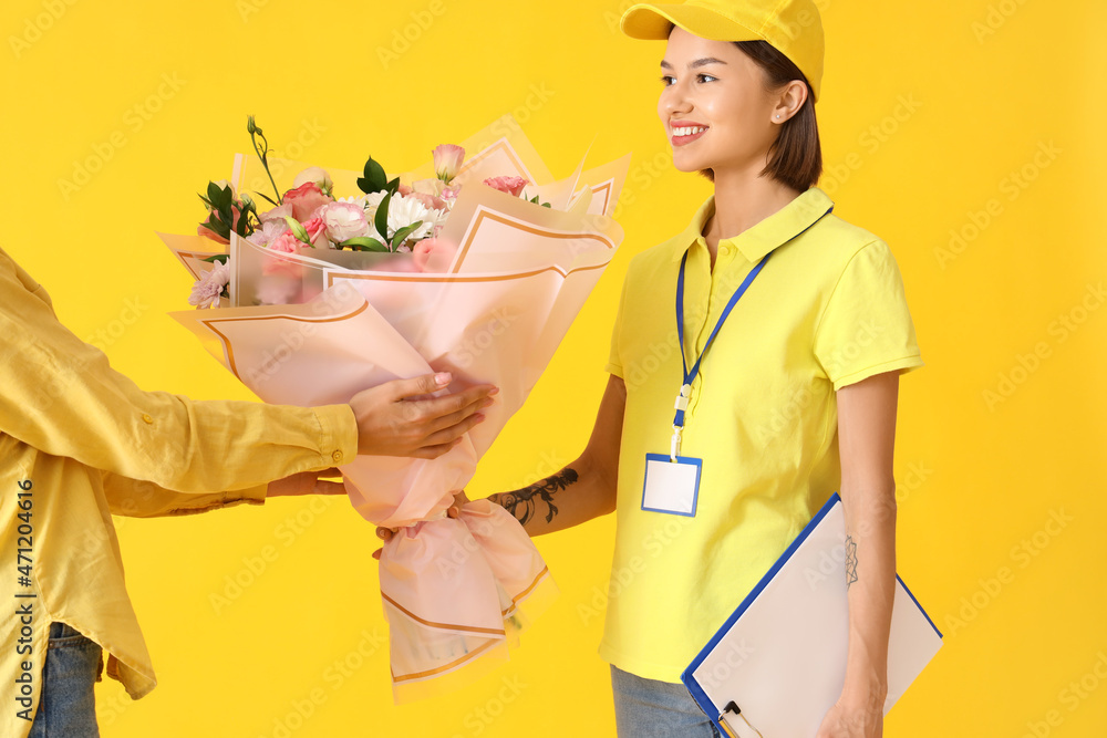 Woman receiving bouquet of flowers from courier on color background
