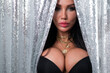 © Михаил Решетников - Portrait of a sexy brunette woman with big breasts dressed in a black bra peeking out from behind curtains of silver sequins.