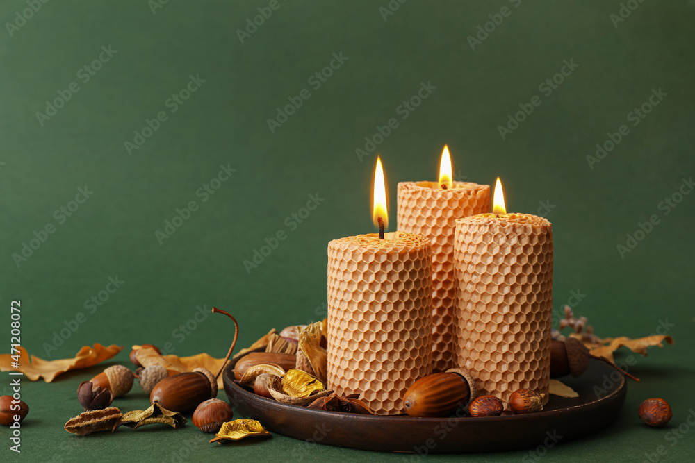 Tray with burning candles and autumn decor on green background