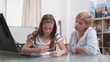 © DC Studio - Mother standing beside daughter helping her with school homework studying mathematics lesson together during coronavirus quarantine. Young children writing exercices on notebook. Distance education