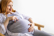 © kostikovanata - Closeup pregnant female holding cute childish booties on huge tummy relaxing at home awaiting baby