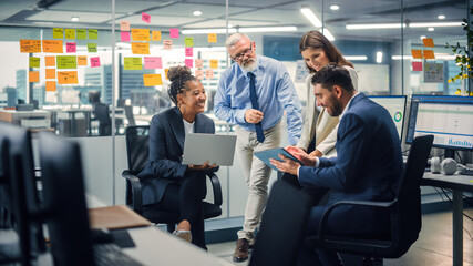 In Modern Office: Diverse Team of Managers Use Laptop and Tablet Computers at a Company Meeting Discussing Business Projects. Young, Motivated and Experienced Employees Brainstorm in Conference Room.