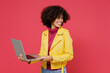 © ViDi Studio - Happy fun businesslike smiling cheery young curly black latin woman 20s years old wears yellow jacket hold use work on laptop pc computer looking back isolated on plain red background studio portrait.