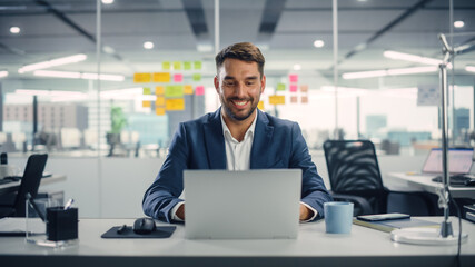 Wall Mural - Busy Young Businessman Using Laptop Computer in Modern Office. Manager Thinks About Successful Financial Ideas. Happy Man Smiling About Finding Problem Solving Solutions for Company.