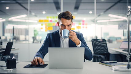 Leinwandbilder - Young Happy Businessman Using Computer in Modern Office with Colleagues. Stylish Handsome Manager Smiling, Working on Financial and Marketing Projects. Drinking Tea or Coffee from a Mug.