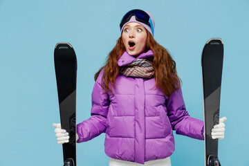 Wall Mural - Skier shocked woman in warm purple padded windbreaker jacket goggles mask spend extreme weekend in mountains look aside on workspace area mock up hold ski isolated on plain blue background studio