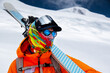 © yanik88 - Mountain portrait of a professional freeride skier in orange clothing with ski poles and skis on his shoulders. Stands high in the mountains on a snowy slope