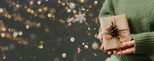Girl Holding Small Gift In Her Hands. Decorated Christmas Tree On Background.