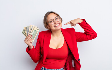 Wall Mural - hispanic pretty woman smiling confidently pointing to own broad smile. business and banknotes concept