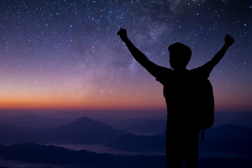 Wall Mural - Silhouette of young traveler standing and open both arm watched night sky view, star and milky way alone on top of the mountain. He enjoyed traveling and was successful when he reached the summit.