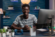 Portrait of smiling african american man using computer while working remote from home at marketing project. Young employee analyzing financial graph sitting at desk using business office technology