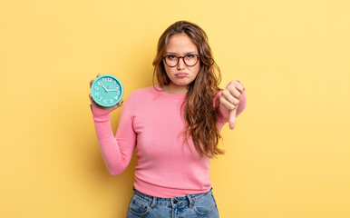 Wall Mural - hispanic pretty woman feeling cross,showing thumbs down. alarm clock concept