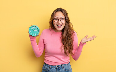 Wall Mural - hispanic pretty woman feeling happy and astonished at something unbelievable. alarm clock concept