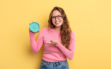 Wall Mural - hispanic pretty woman smiling cheerfully, feeling happy and showing a concept. alarm clock concept