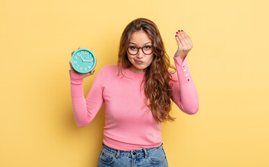 Wall Mural - hispanic pretty woman making capice or money gesture, telling you to pay. alarm clock concept