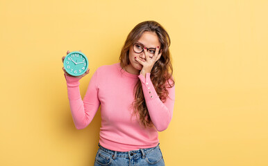 Wall Mural - hispanic pretty woman feeling bored, frustrated and sleepy after a tiresome. alarm clock concept