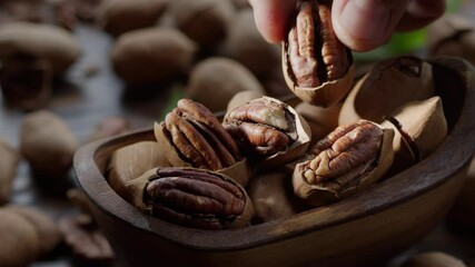 Wall Mural - Pecans in a wooden bowl with pecan leaves and nut shells - close-up video, camera slow motion. The hand takes one of the pecan nut.